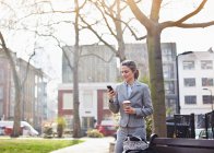 Geschäftsfrau benutzt Handy im Park mit Kaffee — Stockfoto