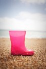 Розовый резиновый сапог на песчаном пляже — стоковое фото