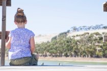 Girl sitting on pier, rear view — Stock Photo