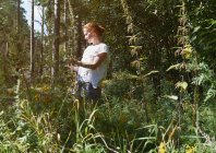 Donna in piedi nella foresta, guardando le piante — Foto stock