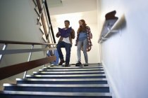 Young male and female college students moving down stairway reading file — Stock Photo