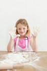 Chica horneando con las manos pegajosas en la cocina - foto de stock