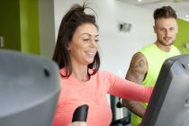 Man and woman in gym using exercise machine smiling — Stock Photo