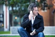 Человек делает телефонный звонок, используя смартфон, сидя на улице — стоковое фото