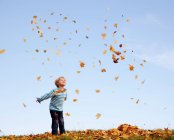 Menino jogando folhas de outono no ar — Fotografia de Stock