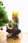 Girl in crown decorating Christmas tree, focus on foreground — Stock Photo
