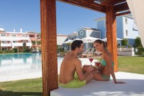 Young couple sitting on sunlounger at holiday resort with cocktails — Stock Photo