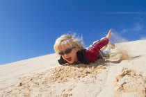 Sonriente niño deslizándose por la duna de arena - foto de stock