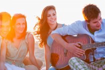 Homem tocando música para amigos na praia — Fotografia de Stock