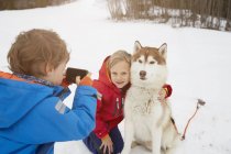 Boy taking smartphone photo of brother and husky in snow, Elmau, Baviera, Alemanha — Fotografia de Stock