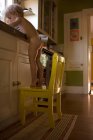 Мальчик стоит на стуле у кухонной раковины — стоковое фото