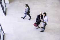 Visão de alto ângulo de dois empresários dirigindo empresária no átrio do escritório — Fotografia de Stock