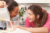Teenage girls measuring milk in kitchen — Stock Photo