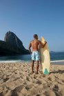 Hombre con tabla de surf en la playa, Rio de Janeiro, Brasil - foto de stock