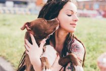 Pit bull terrier licking tattooed young woman in urban park — Stock Photo