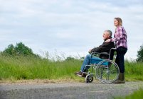 Женщина толкает отца в инвалидном кресле — стоковое фото