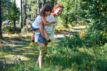 Mother giving daughter piggy back through forest — Stock Photo