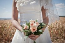 Cropped image of bride in wedding dress holding bouquet in field — Stock Photo