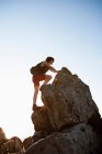 Hiker climbing rocks on hill against blue sky — Stock Photo