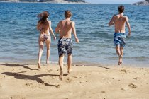 Freunde rennen am Strand ins Meer — Stockfoto