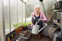 Mature woman holding watering can in greenhouse — Stock Photo