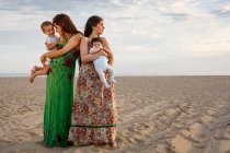 Madres de pie en la playa sosteniendo bebé y niño pequeño - foto de stock