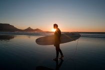 Surfista caminhando na praia ao pôr do sol — Fotografia de Stock