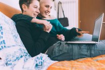 Young lesbian couple reclining on bed pointing at laptop — Stock Photo