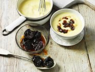 Still life of custard in white bowl, prunes and jam in bowls — Stock Photo