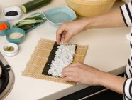 Abgeschnittenes Bild einer Frau beim Zubereiten einer Sushi-Rolle am Tisch — Stockfoto