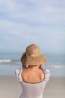 Вид ззаду жінки в солом'яному капелюсі на пляжі — стокове фото