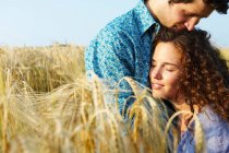 Casal sentado em um campo de trigo, sorrindo — Fotografia de Stock