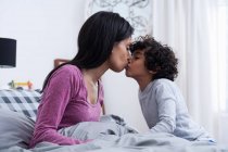 Vista lateral do filho beijando a mãe na cama — Fotografia de Stock