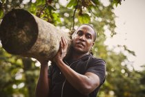 Portrait of mature man training,  lifting tree trunk on shoulder in park — Stock Photo