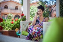 Молодая женщина, отдыхающая во внутреннем дворике квартиры, разговаривая по смартфону, Коста-Рей, Италия — стоковое фото