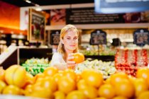 Женщина выбирает апельсин в продуктовом магазине — стоковое фото