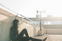Jovem mulher sentada no telhado iluminado pelo sol — Fotografia de Stock