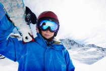 Niño sosteniendo esquís en la montaña nevada - foto de stock