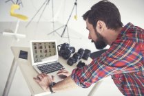Мужчина-фотограф рассматривает фотосессию на ноутбуке в студии — стоковое фото