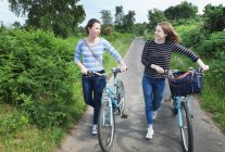 Two young adults pushing bicycles and chatting along country lane — Stock Photo