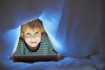 Boy underneath duvet using digital tablet — Stock Photo