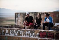 Young men and women sitting on graffiti wall at ruined mine — Stock Photo