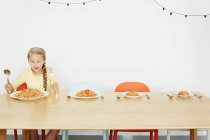 Menina sentada à mesa com espaguete e mais três pratos — Fotografia de Stock