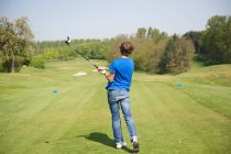 Visão traseira do menino balançando clube no campo de golfe — Fotografia de Stock