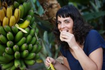 Mujer comiendo plátano fresco recogido y sonriendo - foto de stock