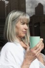 Donna con tazza accanto alla finestra — Foto stock