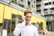 Молодой бизнесмен разговаривает на смартфоне за пределами офиса, Лондон, Великобритания — стоковое фото