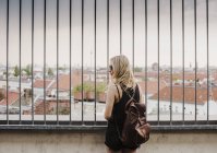 Giovane donna che guarda attraverso le ringhiere, in vista attraverso i tetti, vista posteriore — Foto stock