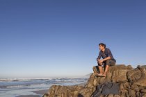 Человек, сидящий на скале у моря — стоковое фото