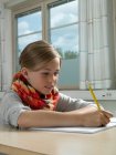 Chica escribiendo en cuaderno de notas con lápiz en un aula - foto de stock